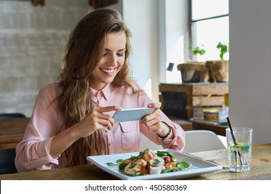 Female blogger photographing lunch in restaurant with her phone