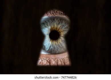 Female blue eye looking through the keyhole. The concept of voyeurism, curiosity, Stalker, surveillance and security