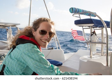 Female Boat Captain In Life Jacket Sits In The Cockpit Of A Sailboat At Sea.