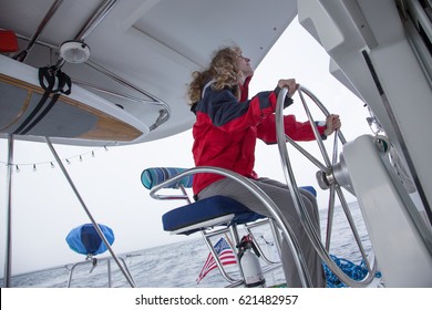 Female Boat Captain Sails Offshore In Rain Jacket At The Helm Of A Sailing Catamaran.