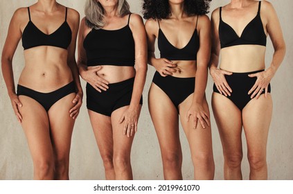 Female Bodies Of All Ages Wearing Black Underwear In A Studio. Group Of Anonymous Women Embracing Their Natural Bodies. Four Body Positive Women Standing Together Against A Studio Background.