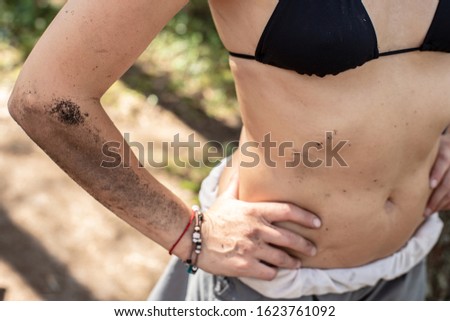 Female body, hand, stomach are dirty with earth and soot from a campfire, in a camp on a sunny summer day.