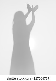female body silhouette creating a shape of a flying bird with her hands, behind a diffuse surface