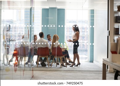 Female boss stands addressing colleagues at business meeting