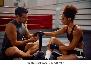 Female boxer applying bandage on her hands with help of a coach in health club.  - Powered by Shutterstock