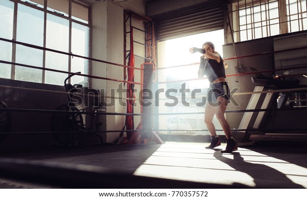 Female boxer doing shadow\
boxing inside a boxing ring. Boxer practicing her punches at a\
boxing studio.