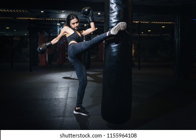 Female Boxer Hitting A Huge Punching Bag At A Boxing Studio. Woman Boxer Training Hard. Thai Boxer Punch Kick By Punching Bag, Black Bacground
