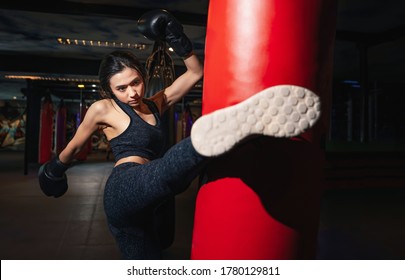 Female Boxer Hitting A Huge Punching Bag At A Boxing Studio. Woman Boxer Training Hard. Thai Boxer Punch Kick By Punching Bag, Black Bacground
