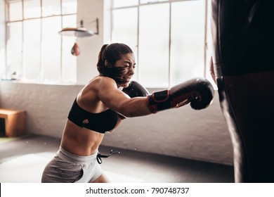 Female boxer hitting a huge punching bag at a boxing studio. Woman boxer training hard. - Powered by Shutterstock