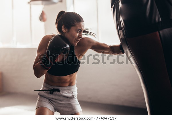 Female boxer hitting a huge punching bag\
at a boxing studio. Woman boxer training\
hard.