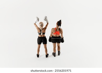 Female boxer raises her hand in victory next to her opponent isolated on white background. Concept of combat sport, martial arts, strength, endurance. Back view - Powered by Shutterstock