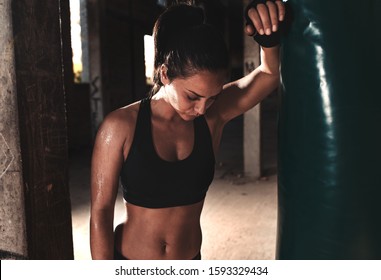 Female boxer resting after punching a boxing bag in warehouse. - Powered by Shutterstock