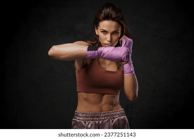 Female boxer in sports bra and shorts, showcasing punching technique with wrapped hands against a dark - Powered by Shutterstock