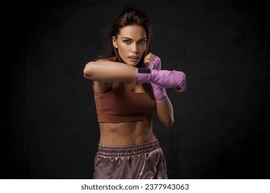 Female boxer in sports bra and shorts, showcasing punching technique with wrapped hands against a dark - Powered by Shutterstock