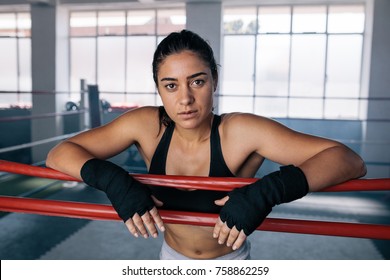 Female boxer standing inside a boxing ring. Boxer resting her arms on the rope of boxing ring. - Powered by Shutterstock