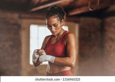 Female boxer wearing strap on wrist. Fitness young woman with muscular body preparing for boxing training at gym.