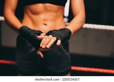 Female boxer wrapping her hands while standing in a boxing ring. Athletic young woman preparing for a boxing training session in a fitness gym. - Powered by Shutterstock