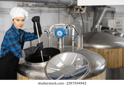 Female brewer is controls the brewing process near reservoir with beer indoor - Powered by Shutterstock