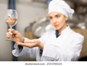 Female brewmaster standing in beer factory and holding glass of malt. Out of focus woman. - Powered by Shutterstock