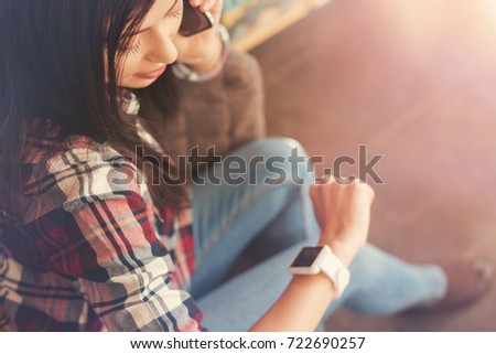 Female brunette freelancer looking on wrist watch during phone talk