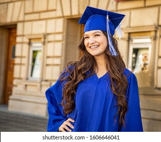 Female Brunette Latino College Or High School Graduate Smiling Confidently Wearing  Blue Cap And Gown At Graduation. Negative Space On The Left Of The Image