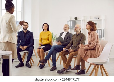 Female business coach speaks in front of small group of business people teaching them new business knowledge. Satisfied different people sitting on chairs in row and listening to dark skinned woman. - Powered by Shutterstock