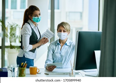 Female Business Colleagues With Face Masks Working In The Office And Reading An E-mail On A Computer. 