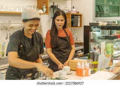 Female Business Owner Works With Her Partner To Prepare Coffee Or Drink For Customer In A Coffee Shop. A Couple Of LGBT Startup Help Each Other At A Coffee Counter For Their Business.