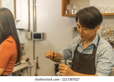 Female Business Owner Works With Her LGBT Partner To Prepare Coffee Or Drink For Customer In A Coffee Shop. A Couple Of LGBT Startup Help Each Other At A Coffee Counter For Their Business.