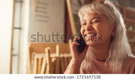 Female Business Owner In Workshop Making Call On Mobile Phone