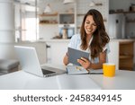 Female business person using digital tablet and laptop or remote working at home office, looking at digital tablet watching webinar, learning training, studying online seminar or video calling.