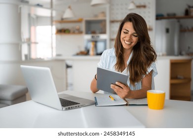 Female business person using digital tablet and laptop or remote working at home office, looking at digital tablet watching webinar, learning training, studying online seminar or video calling.