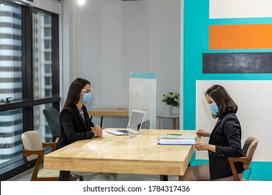 Female Business Workers Wearing Face Mask And Shield Making A Business Deal Or Discussion Through Glass Partition At The Office As Part Of Business In New Normal And Social Distancing During COVID-19