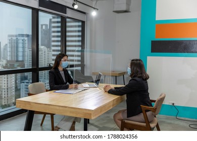 Female Business Workers Wearing Face Mask And Clear Shield Having Discussion Through Glass Partition At The Office As Part Of Business In New Normal During The Outbreak Of COVID-19 Or Coronavirus