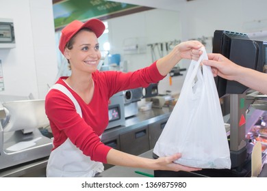 Female Butcher Giving Bag To Customer At Shop Counter