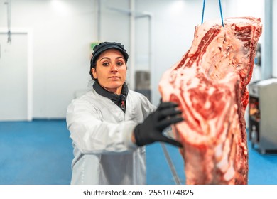 Female butcher in uniform and protective gloves working transporting hanged meat on meat processing factory - Powered by Shutterstock