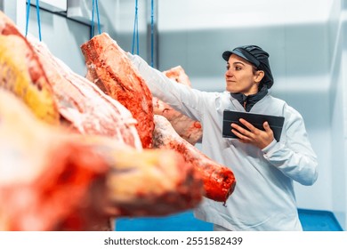 Female butcher using digital tablet to analyze products in a cold meat storage room - Powered by Shutterstock