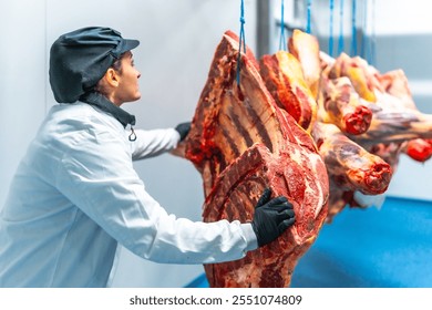 Female butcher working in a cold storage room of a meat processing factory carrying hanged pieces of meat - Powered by Shutterstock