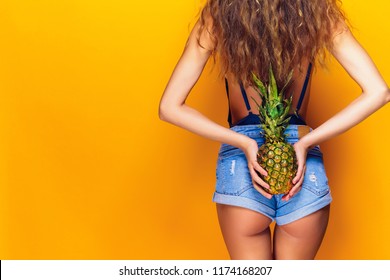 Female Buttocks, Sexy Ass. Young Sporty Woman Holding A Pineapple In Her Hand. On A Yellow Background.