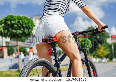 Female buttocks in white shorts on a bicycle saddle on a bicycle ride in the park on a background of ornamental trees.