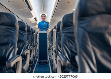 Female Cabin Attendant Leading Trolley Cart Through Empty Plane Aisle. Travel, Service, Transportation, Airplane Concept