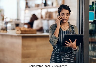 Female cafe business owner using phone talking, ordering and reading on tablet in her store. Serious businesswoman, entrepreneur or employee standing in a coffee shop preparing online grocery order. - Powered by Shutterstock