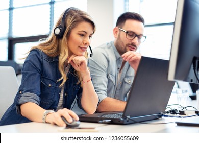 Female Call Center Operator Working With Her Headset On. Supervisor Is Sitting Next To Her.