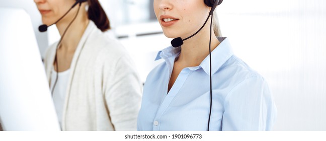 Female call operator is using computer and headset for consulting clients online, close-up. Group of diverse people working as customer service occupation