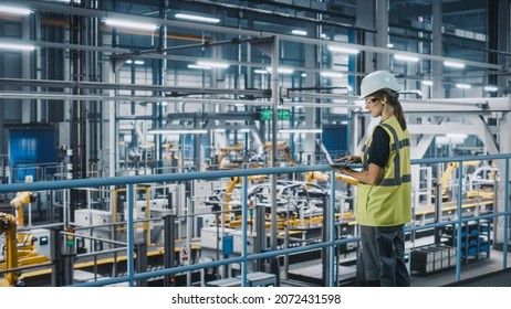 Female Car Factory Engineer in High Visibility Vest Using Laptop Computer. Automotive Industrial Manufacturing Facility Working on Vehicle Production with Robotic Arms. Automated Assembly Plant. - Shutterstock ID 2072431598