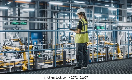 Female Car Factory Engineer in High Visibility Vest Using Laptop Computer. Automotive Industrial Manufacturing Facility Working on Vehicle Production with Robotic Technology. Automated Assembly Plant. - Shutterstock ID 2072431607