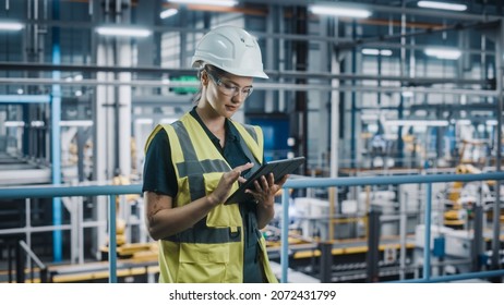 Female Car Factory Engineer In High Visibility Vest Using Laptop Computer. Automotive Industrial Manufacturing Facility Working On Vehicle Production With Robotic Arms. Automated Assembly Plant.