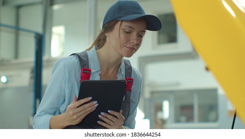 Female car mechanic using a digital tablet while doing routine maintenance check-up on a car in a garage. - Shutterstock ID 1836644254
