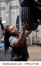 Female Car Mechanic Worker Checking, Repair And Maintenance Wheel At Auto Repair Shop. African Woman Mechanic Vehicle Service Maintenance Examining Wheel Tire At Garage. Auto Car Repair Service