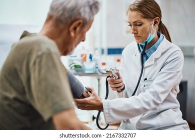 Female Cardiologist Measuring Blood Pressure Of A Senior Patient During Medical Exam At Doctor's Office.